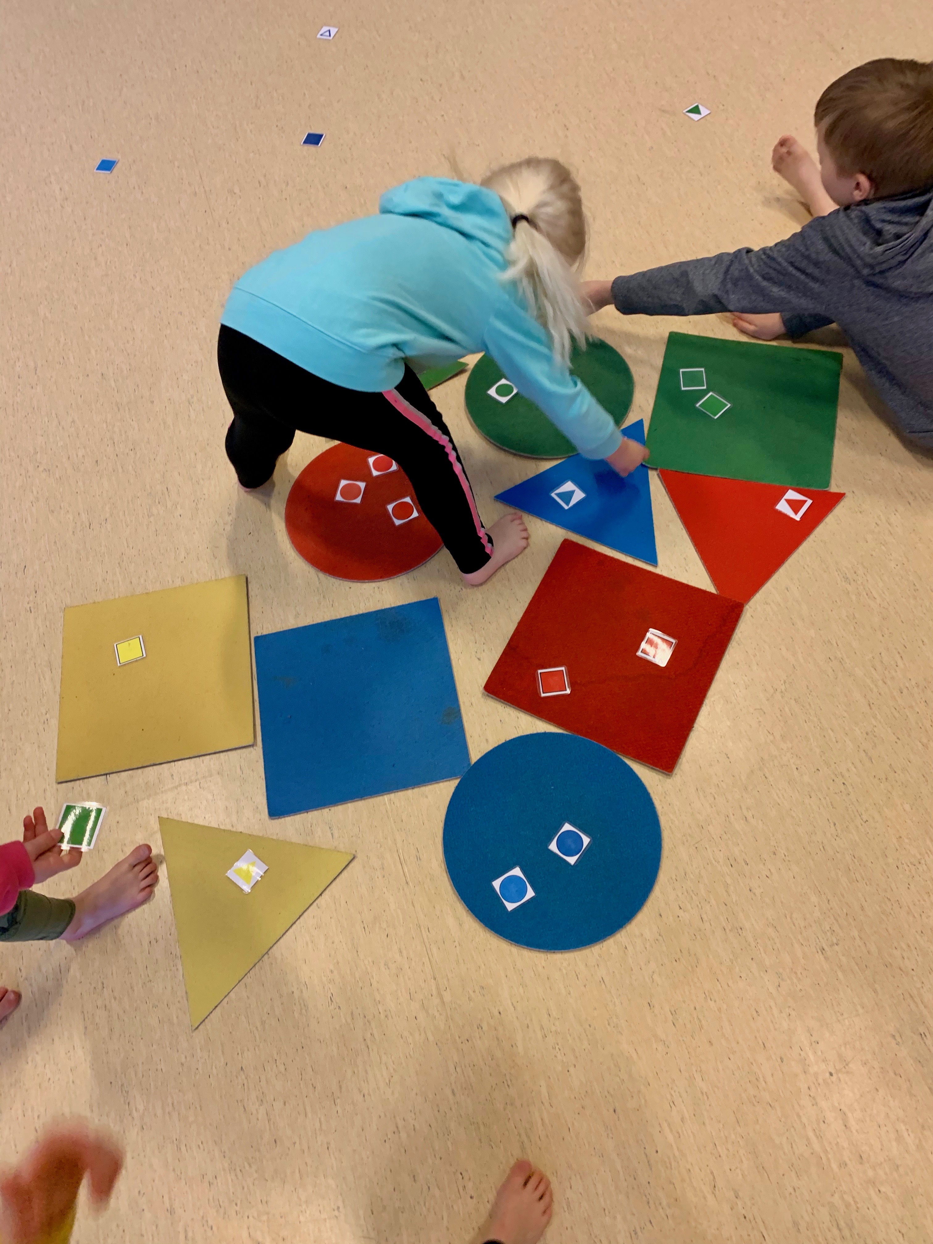 Lapsia leikkimässä värikkäiden kartonkimuotojen kanssa.